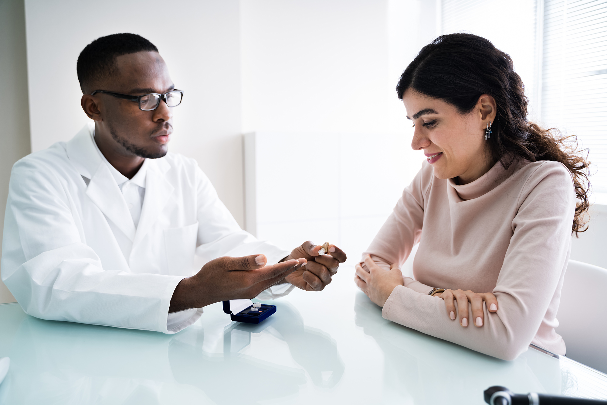 Close-up Of Doctor Showing Hearing Aid To Patient